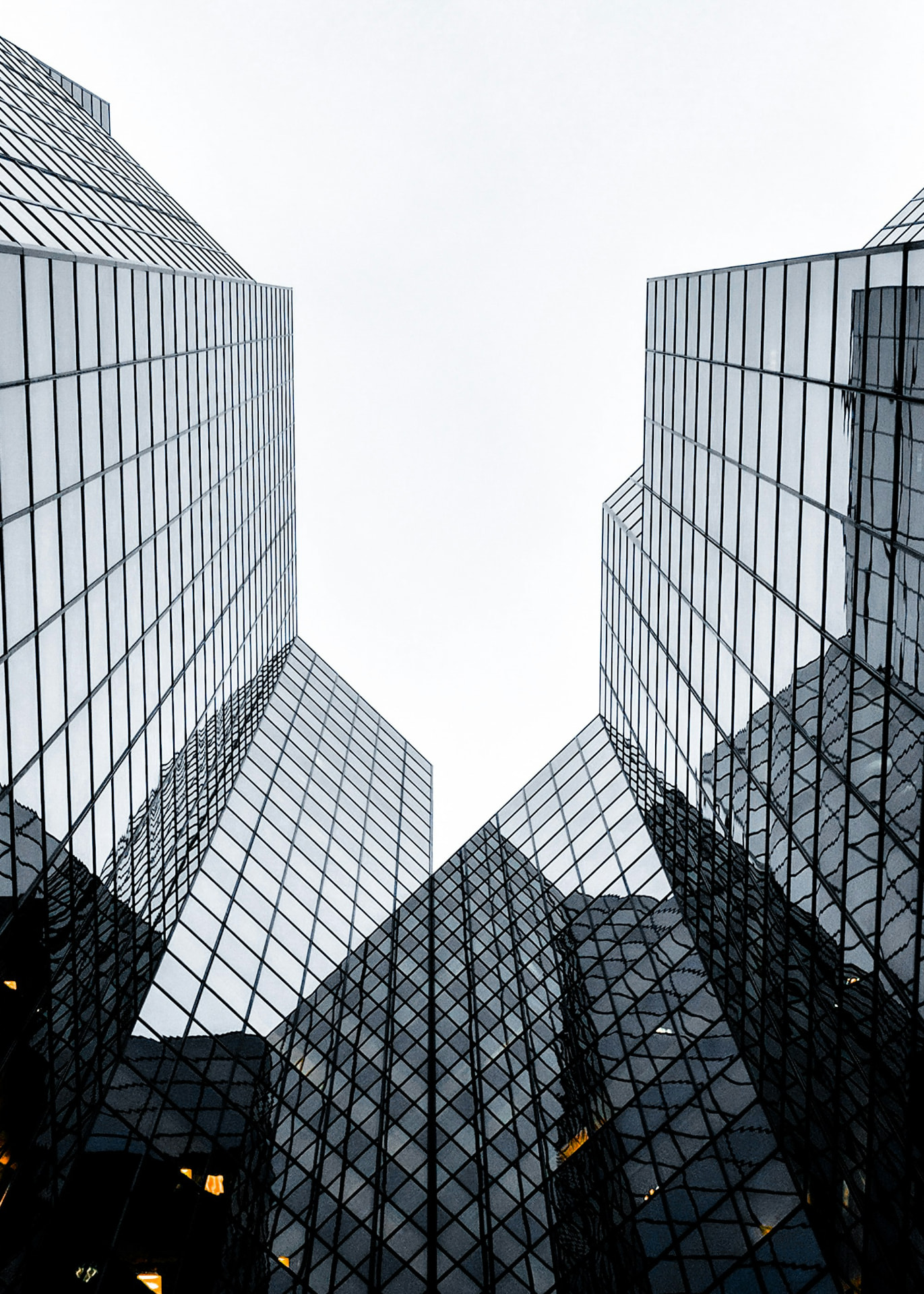 Two glass office towers viewed from below, converging toward the sky