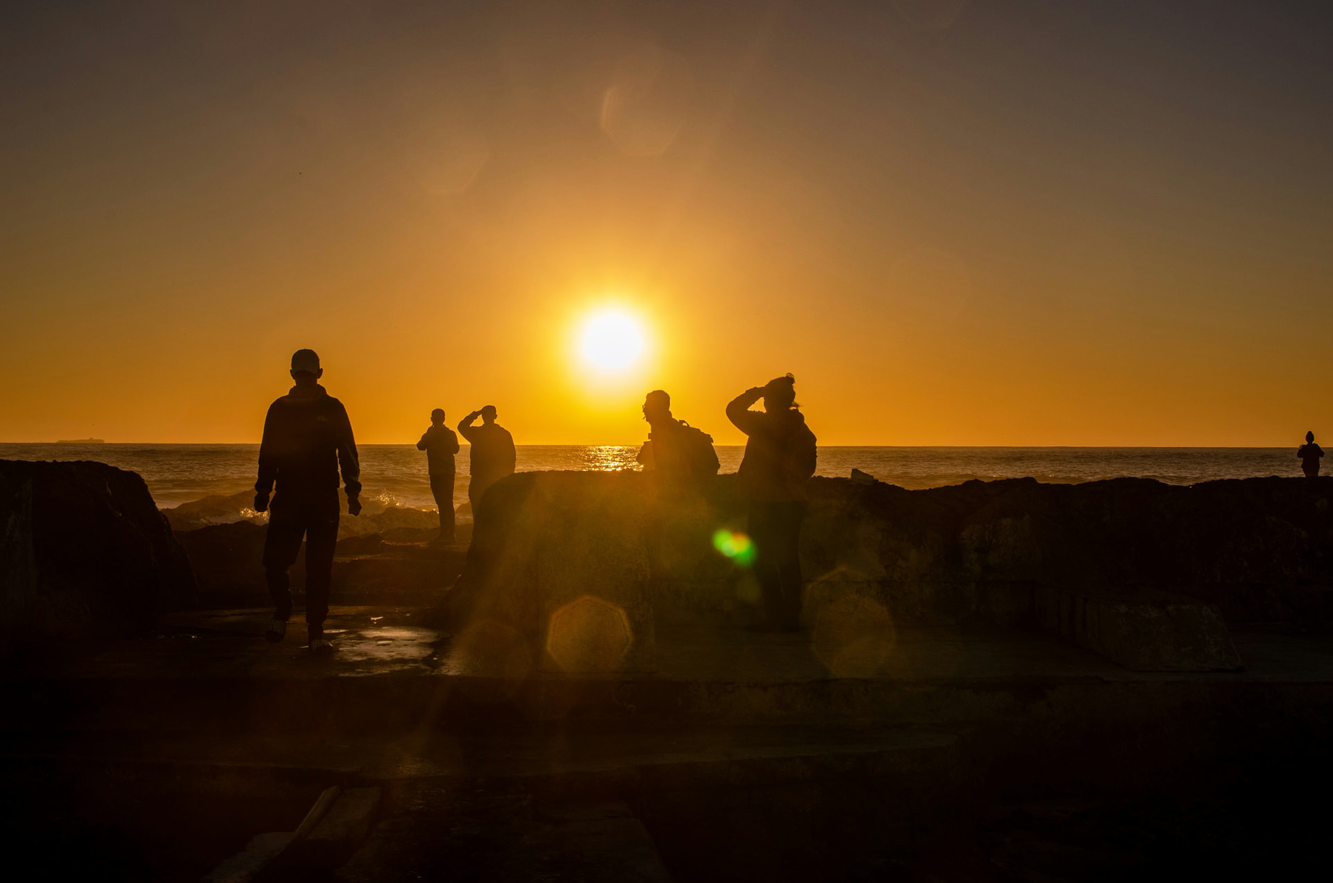 People silhouetted on a rocky shoreline watching the sun set over the sea
